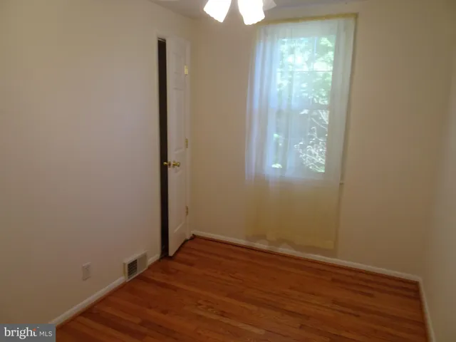 an empty room with wooden floor exposed radiator and a ceiling fan
