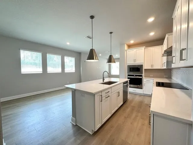 a large kitchen with stainless steel appliances granite countertop a sink a stove a refrigerator and island with wooden floor