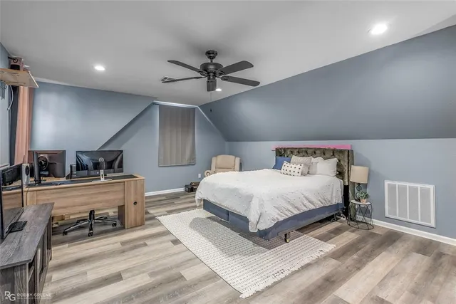 a bedroom with a bed a dresser and potted plants with wooden floor