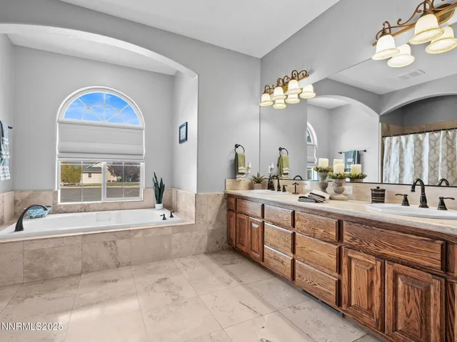 a bathroom with a double vanity sink a mirror a bathtub and a window