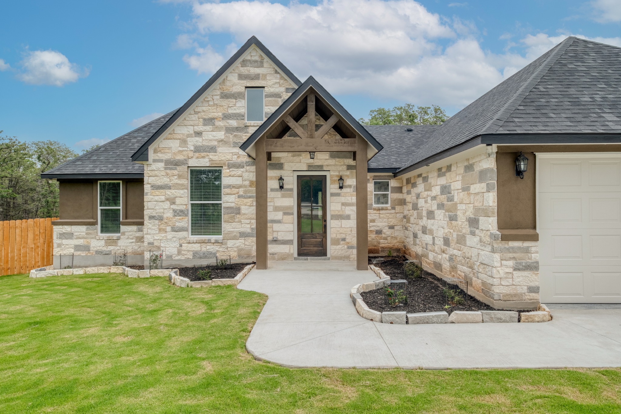 116 Pine Point Cove Elgin, TX 78621 - Photo 4 of 27 Stone facade entry with a dark wood-finish door, covered porch with exposed timber framing, and a two-car garage