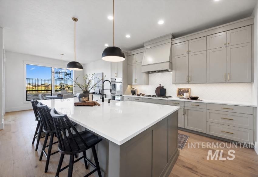 5847 South Pinpoint Way Meridian, ID 83642 - Photo 20 of 44 Kitchen featuring an oversized island with countertop seating, light wood-finish flooring, a contemporary range hood, and pendant lighting