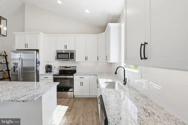 a kitchen with granite countertop a sink stainless steel appliances and white cabinets