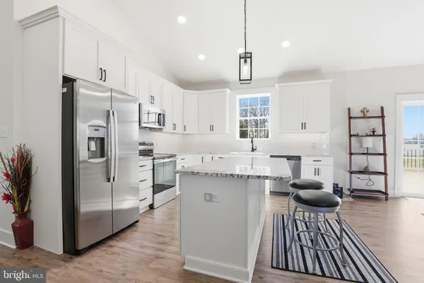a kitchen with stainless steel appliances kitchen island granite countertop a refrigerator a oven a stove and white cabinets with wooden floor