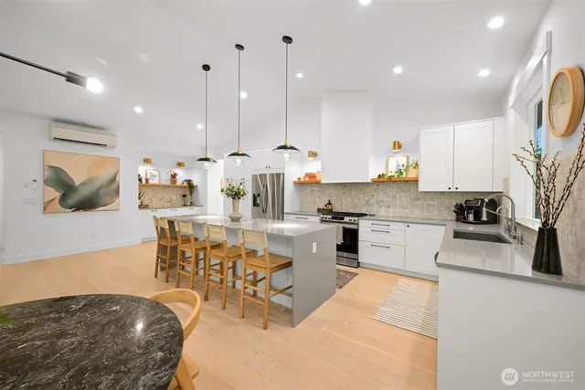a kitchen with stainless steel appliances kitchen island granite countertop a stove a sink a microwave a dining table and chairs with wooden floor