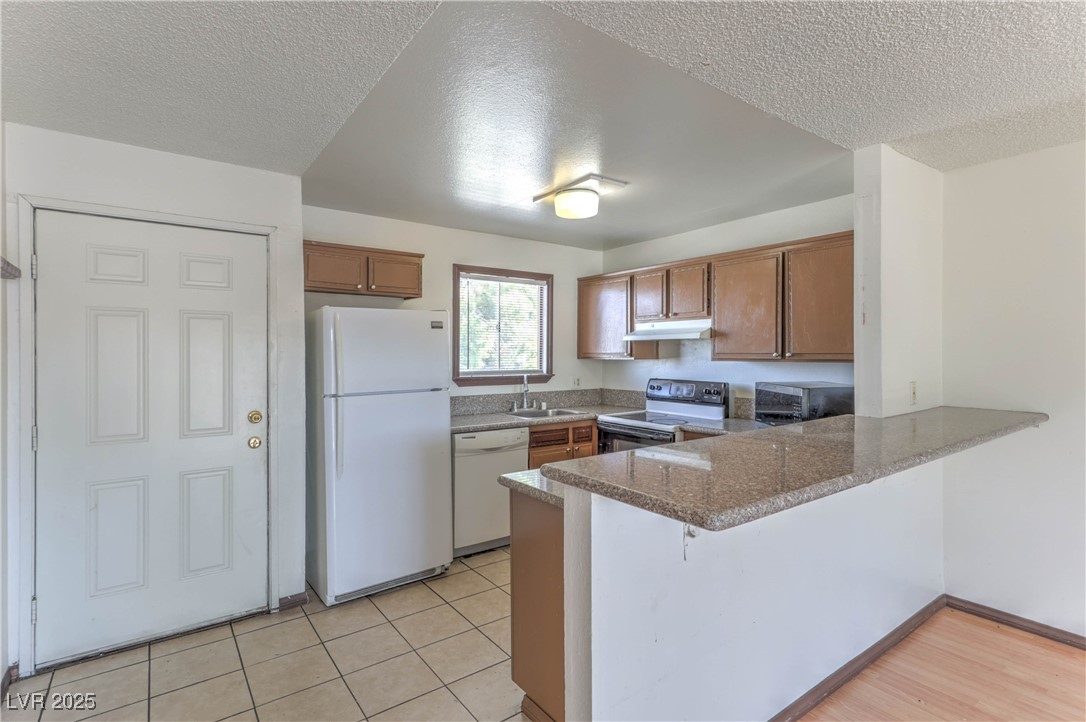 5404 South Swenson Street, Unit 34 Las Vegas, NV 89119 - Photo 4 of 28 Kitchen with a peninsula, white appliances, brown cabinetry, a breakfast bar area, and a textured ceiling