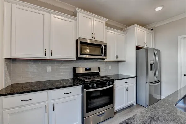 a kitchen with stainless steel appliances granite countertop white cabinets sink and a refrigerator