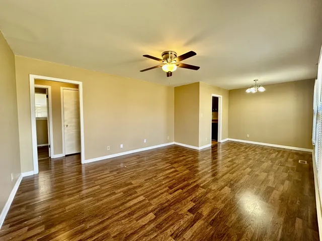 a view of an empty room and kitchen with wooden floor