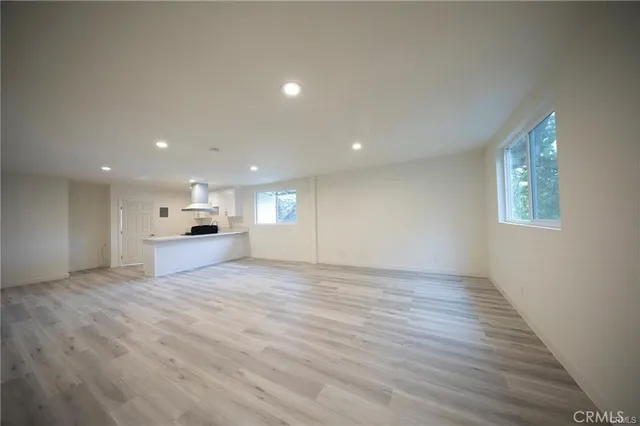 a view of empty room with wooden floor and kitchen