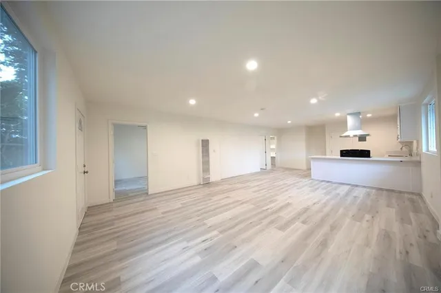 a view of empty room with wooden floor and kitchen