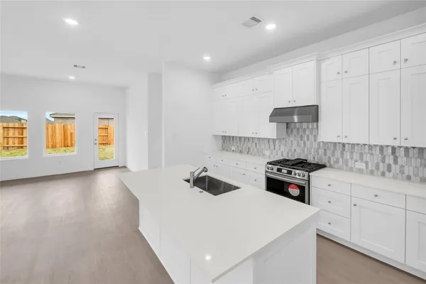 a kitchen with stainless steel appliances a stove a sink a refrigerator white cabinets and wooden floor