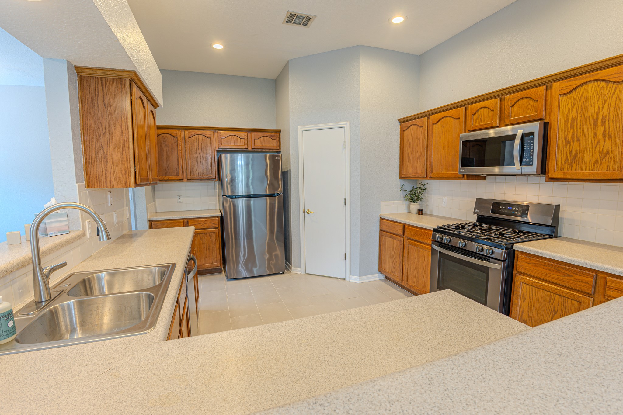 208 Discovery Kyle, TX 78640 - Photo 11 of 31 Kitchen featuring wood cabinetry, stainless steel appliances, a double basin sink, light-toned countertops, and a white subway tile backsplash