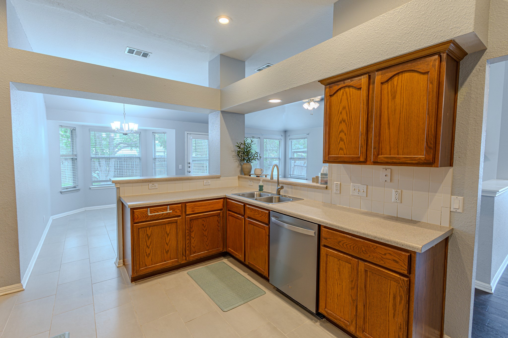 208 Discovery Kyle, TX 78640 - Photo 14 of 31 Kitchen featuring wood cabinetry, light-toned countertops, a stainless steel dishwasher, and a tile backsplash