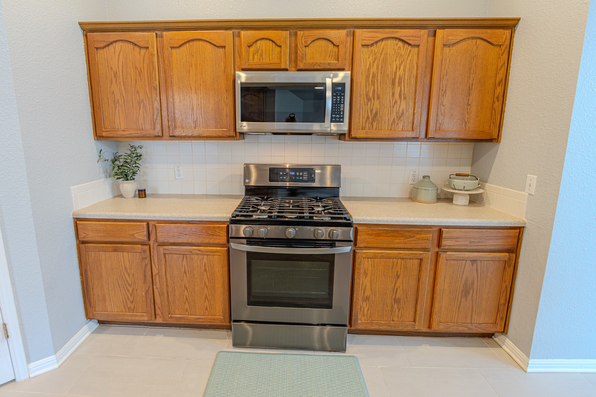 208 Discovery Kyle, TX 78640 - Photo 15 of 31 Kitchen featuring wood-finish cabinetry, stainless steel range with gas cooktop, stainless steel microwave, light-colored countertops, and white subway tile backsplash