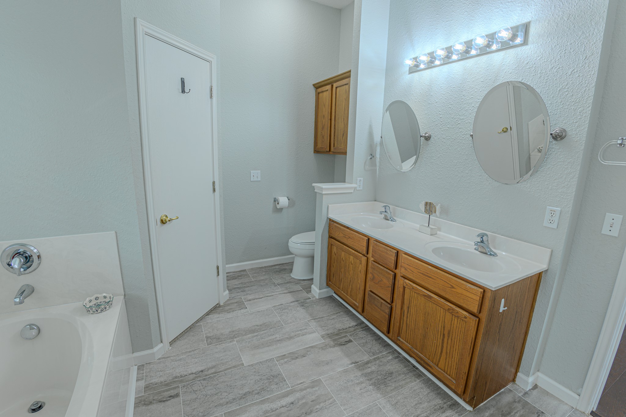 208 Discovery Kyle, TX 78640 - Photo 19 of 31 Spacious bathroom featuring a double vanity with wood cabinetry and a white countertop, two oval mirrors, and a built-in soaking tub