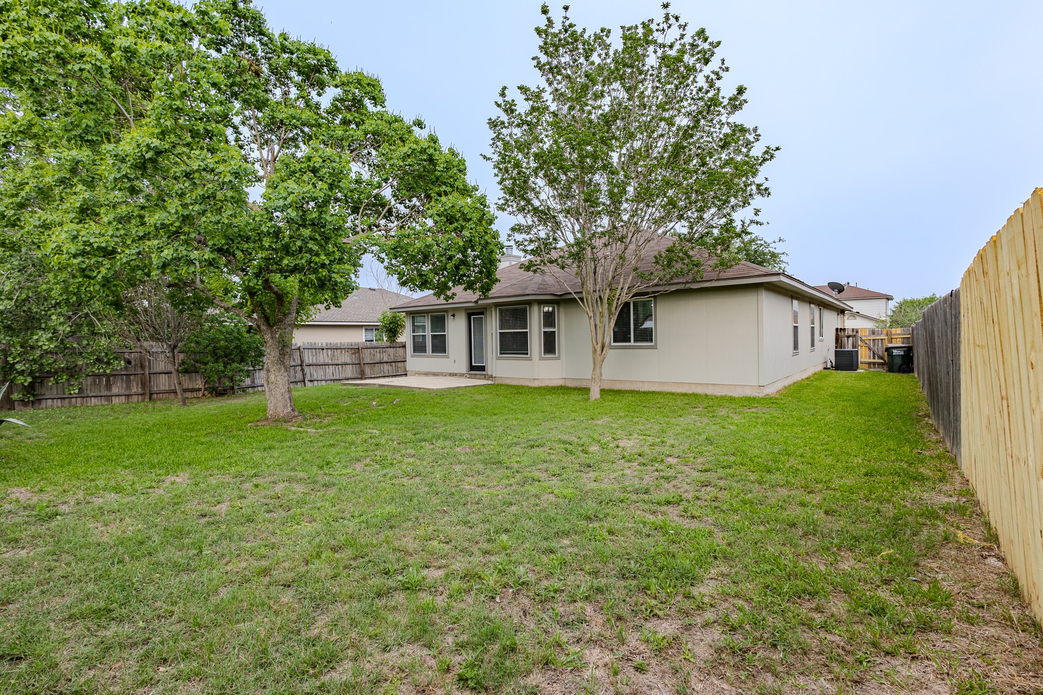 208 Discovery Kyle, TX 78640 - Photo 30 of 31 Expansive grassy backyard featuring a concrete patio, mature trees, and a combination of wood panel and picket fencing