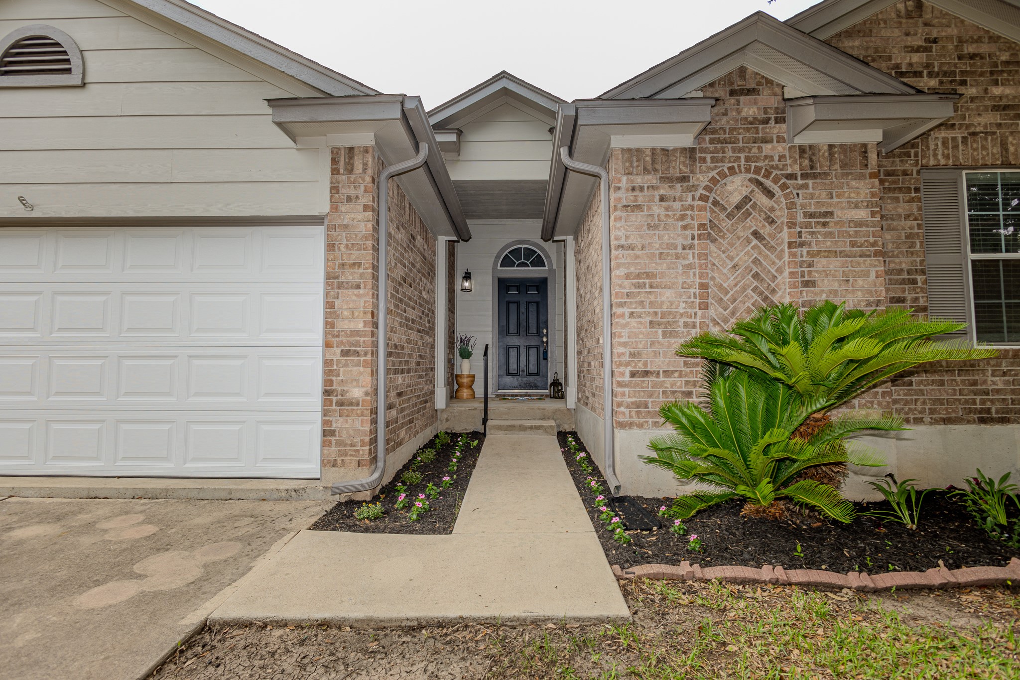 208 Discovery Kyle, TX 78640 - Photo 5 of 31 Brick and siding exterior featuring a paneled garage door, arched entry door with sidelights, a concrete walkway, and landscaped garden beds