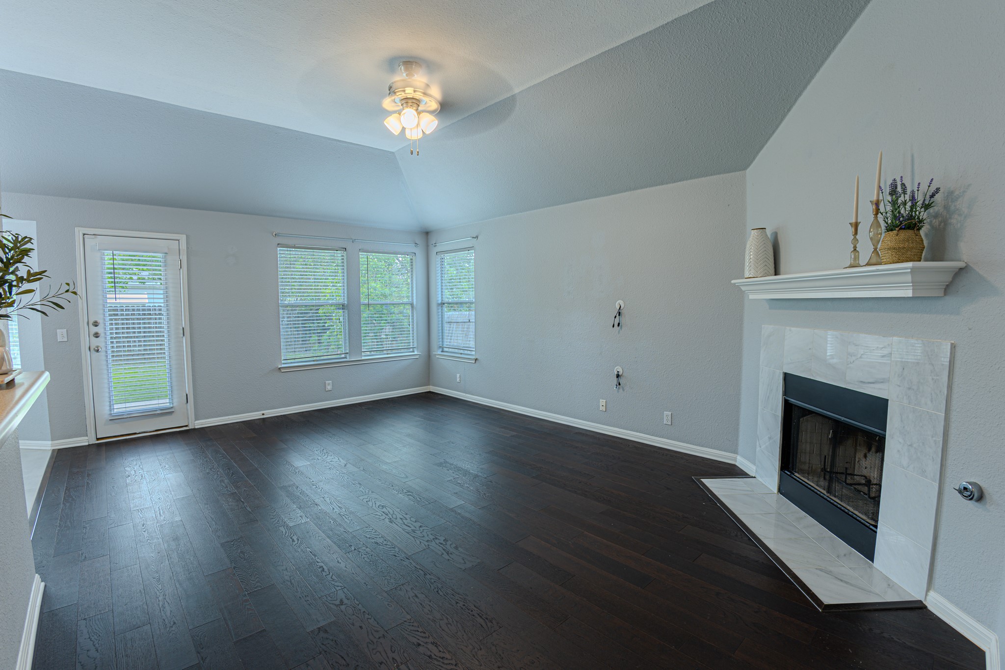 208 Discovery Kyle, TX 78640 - Photo 8 of 31 Spacious living area featuring dark wood-finish flooring, a white-tiled fireplace with mantel, and vaulted ceilings