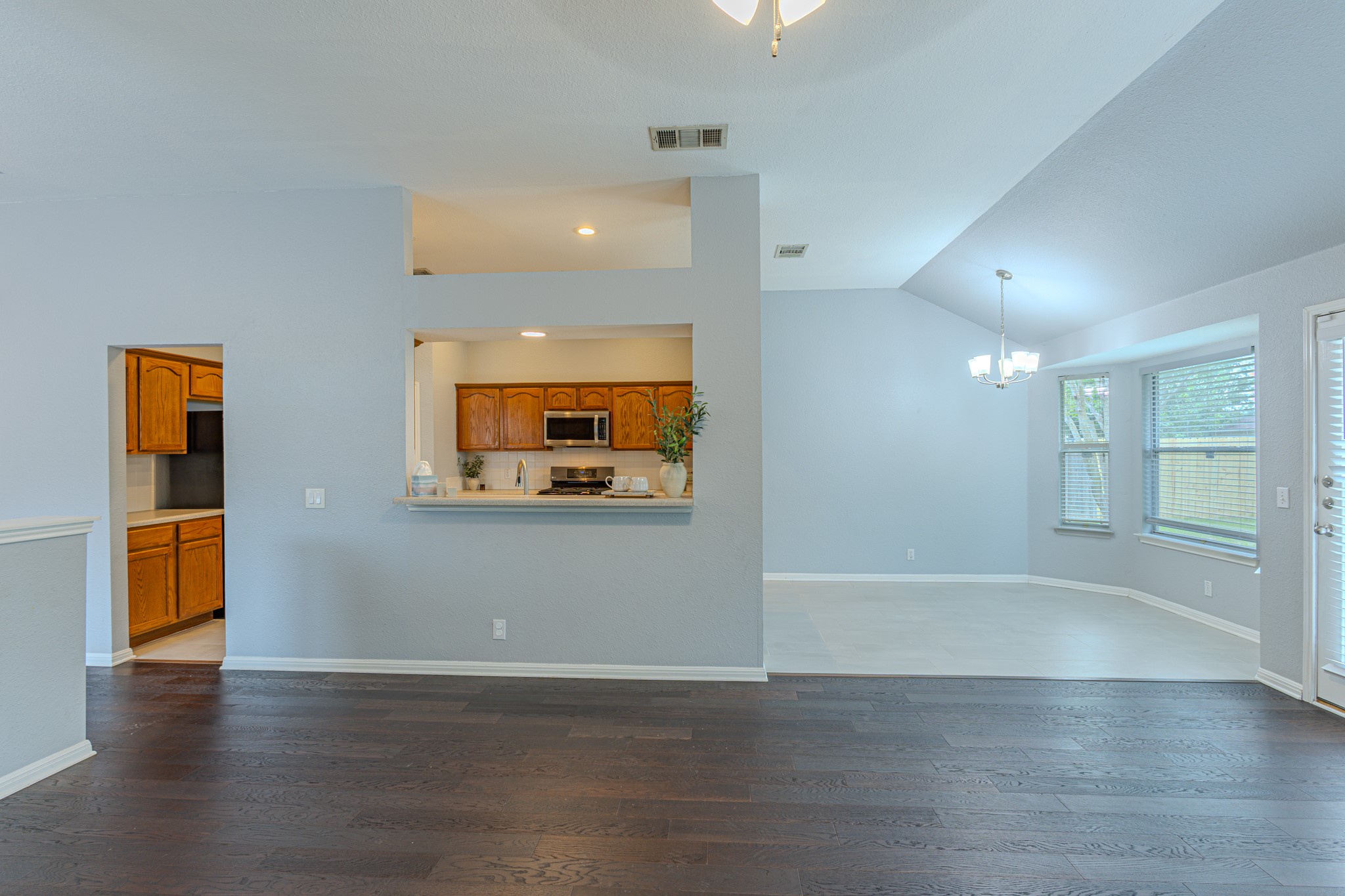 208 Discovery Kyle, TX 78640 - Photo 10 of 31 Open-concept living area featuring dark wood-finish flooring, a kitchen pass-through with a breakfast bar, and a dining area with a bay window
