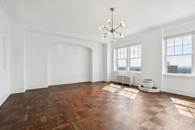 a view of an empty room with window and chandelier fan