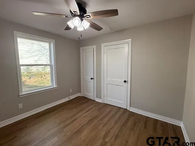 an empty room with wooden floor chandelier fan and windows