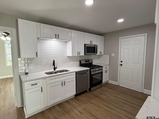 a kitchen with a sink cabinets stainless steel appliances and wooden floor