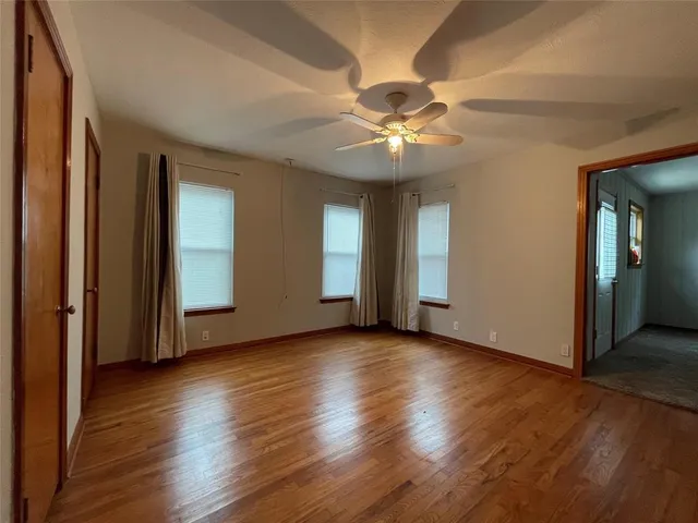 an empty room with wooden floor chandelier fan and windows