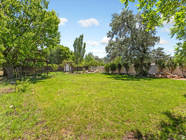 12825 South Fort Street Draper, UT 84020 - Photo 34 of 52 Expansive green lawn with mature shade trees, a perimeter fence, garden arbor, and a fire pit area