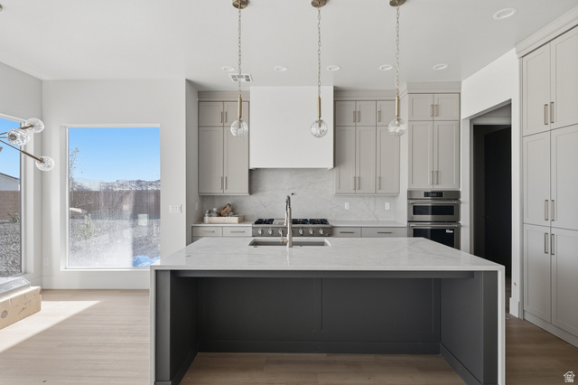 3011 East Rimrunner Drive, Unit 302 St. George, UT 84790 - Photo 12 of 45 Dual tone kitchen featuring light stone countertops, a center island with sink, light wood finished floors, hanging light fixtures, and two tone cabinets