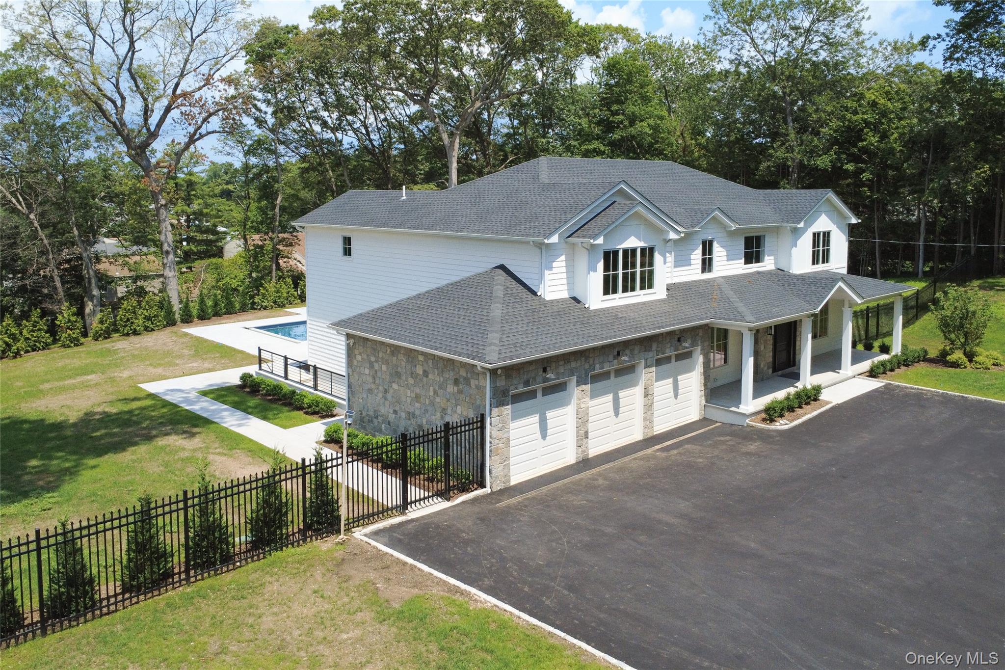 32 A Pine Road Syosset, NY 11791 - Photo 3 of 46 View of front of house featuring driveway, covered porch, stone siding, a shingled roof, and view of wooded area