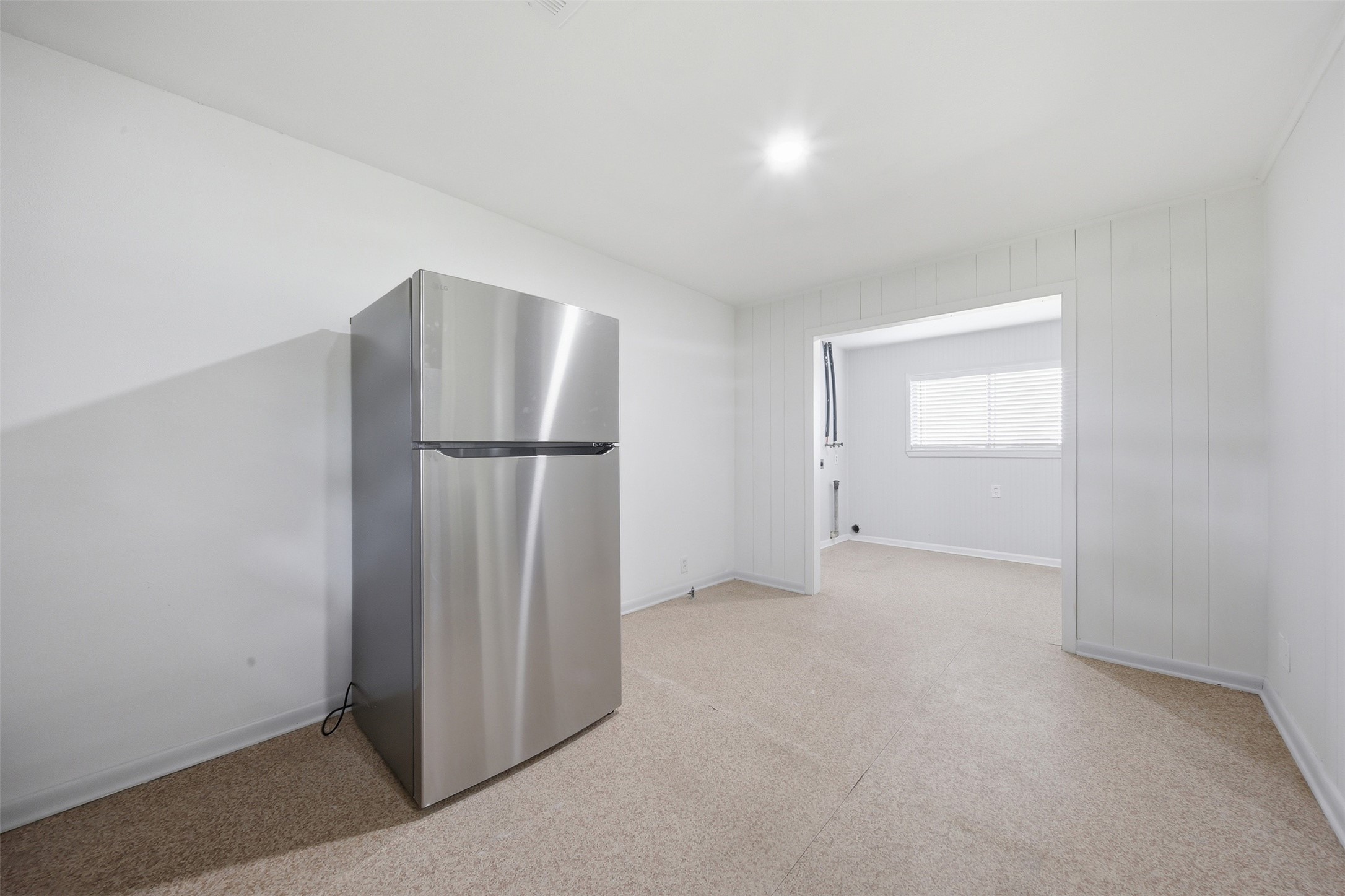 5443 Randon School Road Rosenberg, TX 77471 - Photo 9 of 20 Rear entry area with stainless refrigerator, neutral flooring, white paneled walls, and open access to the utility room.
