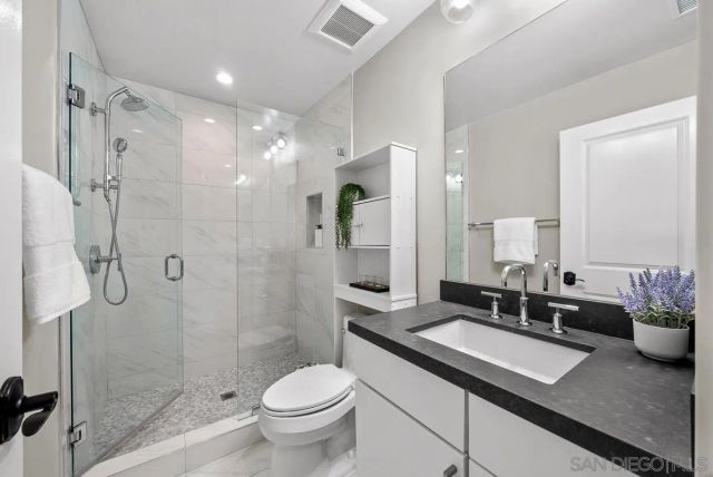 a bathroom with a granite countertop sink a toilet a mirror and shower