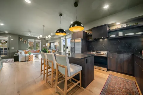 a kitchen with stainless steel appliances granite countertop a stove a sink a refrigerator white cabinets and couches with wooden floor