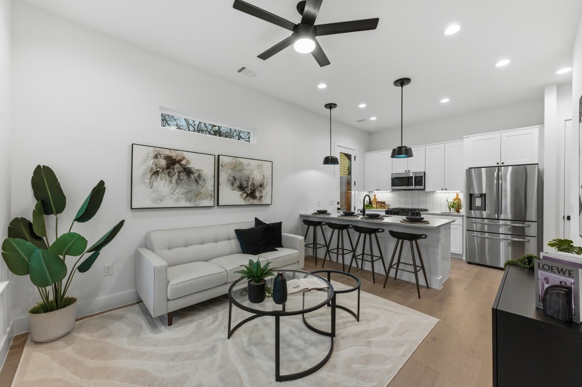 Living area with light wood-style floors, recessed lighting, and a ceiling fan.