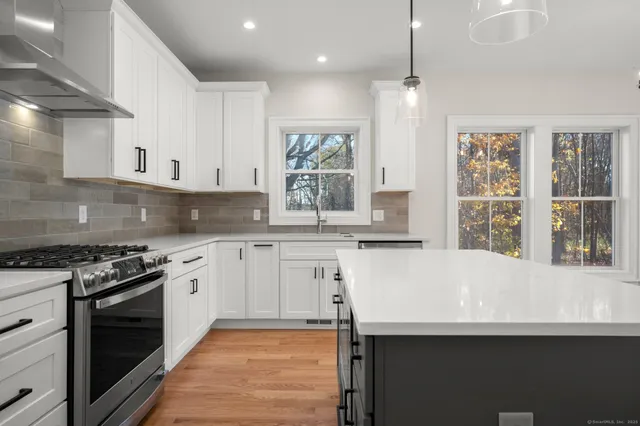 a large kitchen with granite countertop a white stove top oven and white cabinets with wooden floor
