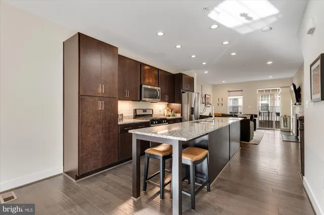 a kitchen with stainless steel appliances granite countertop a refrigerator a sink dishwasher a stove and a refrigerator with wooden floor