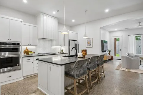 a kitchen with stainless steel appliances granite countertop a stove top oven a sink a dining table and chairs with white cabinets