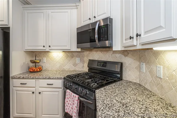 a kitchen with stainless steel appliances granite countertop white cabinets and a stove top oven