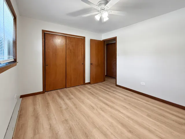 a view of an empty room with wooden floor and a ceiling fan