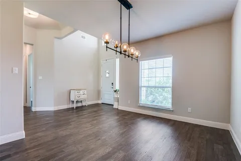 a view of an empty room with wooden floor and a kitchen