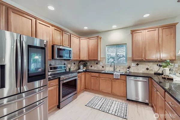 a kitchen with stainless steel appliances granite countertop white cabinets a sink dishwasher a stove and a refrigerator with wooden floor