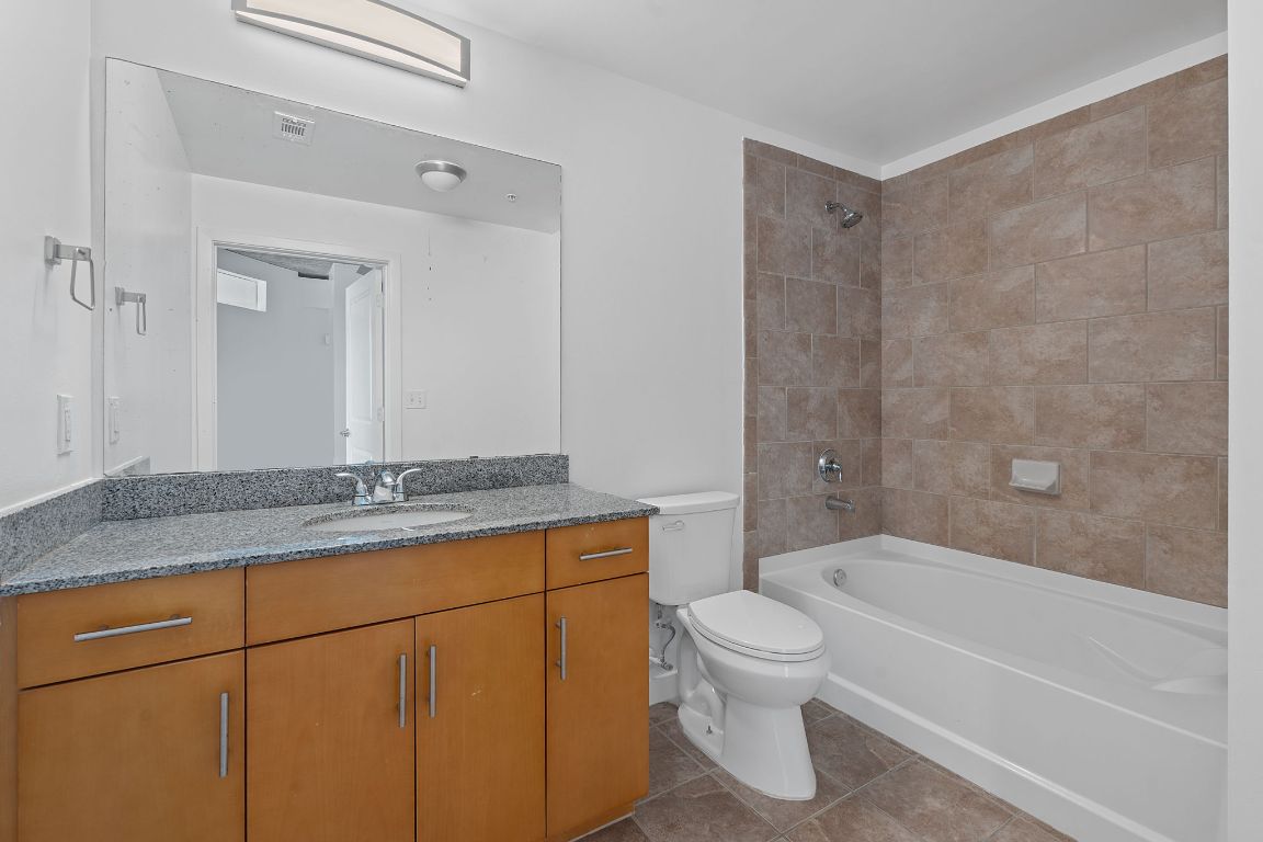 360 Nueces Street, Unit 2401 Austin, TX 78701 - Photo 22 of 40 a bathroom with a granite countertop bathtub shower sink mirror and toilet