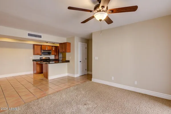 an empty room with kitchen view and a ceiling fan