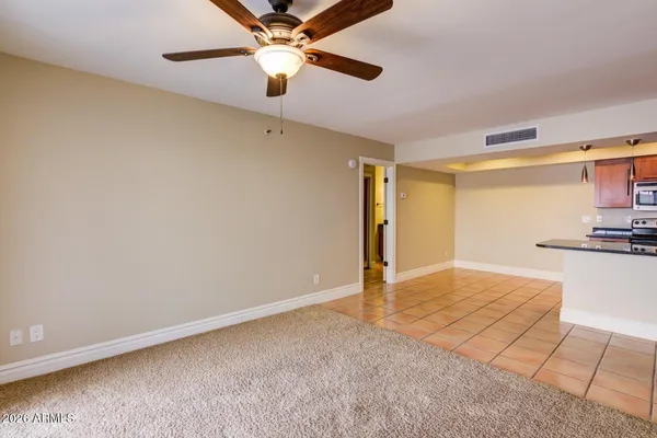 an empty room with kitchen view and a ceiling fan