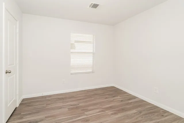 a view of an empty room with wooden floor and a window