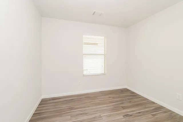 a view of an empty room with wooden floor and a window