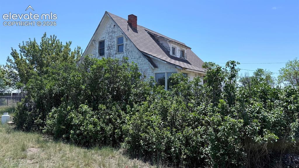 3380 Curtis Road Peyton, CO 80831 - Photo 3 of 13 White clapboard siding exterior with a dark shingle roof and a red brick chimney