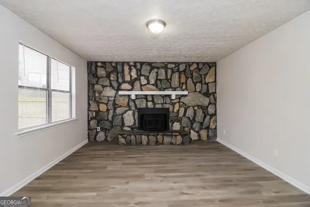 an empty room with wooden floor fireplace and windows