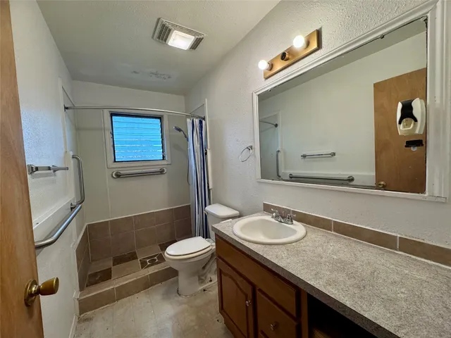 a bathroom with a granite countertop sink a toilet a mirror and shower