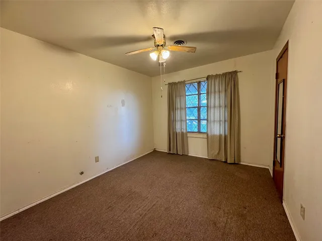 an empty room with chandelier fan and windows